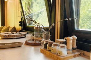 A room with a wooden table, jars of candles, a salt and pepper set, and a window with a view of greenery. - Pana Ayusai (Almaty)