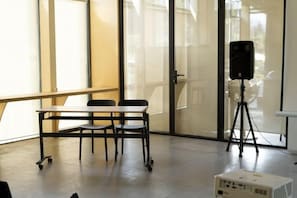 A conference room with a table, chairs, a projector on a tripod, and a speaker. - Pana Ayusai (Almaty)