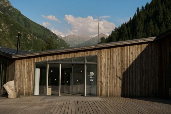 Un edificio de madera con acceso de vidrio, frente a una imponente cordillera.