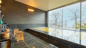 Un moderno espacio de spa con una bañera grande, taburetes de madera y vistas a árboles a través de amplios ventanales.