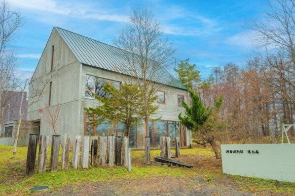 A two-story building with a metal roof, surrounded by a wooden fence, and a sign with text. - Toyako Villa Susukian (Usu District)