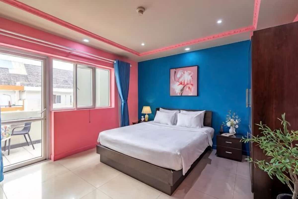 A bedroom with a bed, bedside table, lamp, and a view through a window.