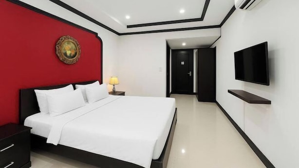 A modern hotel room with a large bed, a flat-screen TV, a red accent wall, and a ceiling-mounted air conditioner. - La Serena Boutique Hotel (Ho Chi Minh City)