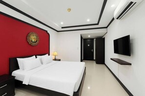 Une chambre d’hôtel moderne dotée d’un grand lit, d’un téléviseur à écran plat, d’un mur d’accent rouge et d’un climatiseur fixé au plafond.