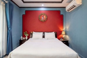 A hotel room with a large bed, a nightstand with a lamp, and a wall-mounted air conditioner.