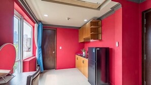 A compact kitchen with a refrigerator, wooden cabinets, and a window with a curtain. - La Serena Boutique Hotel (Ho Chi Minh City)