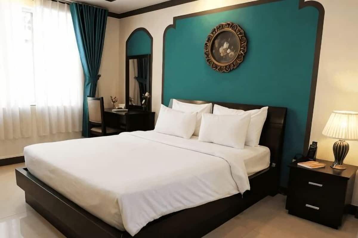 A hotel room with a large bed, a nightstand, a lamp, and a wall-mounted mirror.