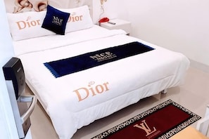 Une chambre d’hôtel avec un lit orné de la marque « Dior », une table de chevet avec un téléphone rouge et un tapis à carreaux rouges et noirs.