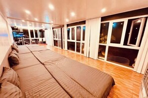 A long, narrow room with a row of beds along one wall, large windows, and a wooden floor. - Nice Hotel Buon Ma Thuot (Tu An)