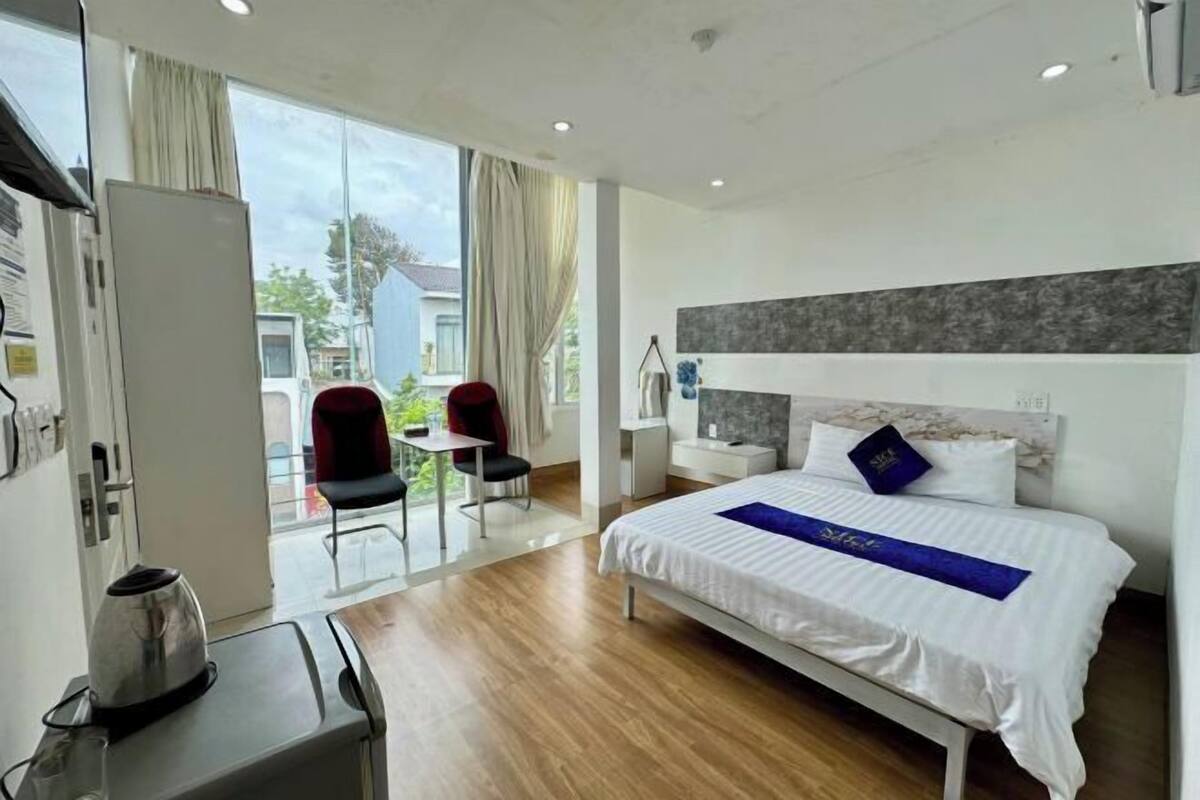 A hotel room with a bed, a desk, a chair, and a view of the outside.