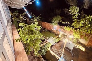 Une vue nocturne d’une cour intérieure avec un élément décoratif aquatique, un mur de briques et quelques plantes.