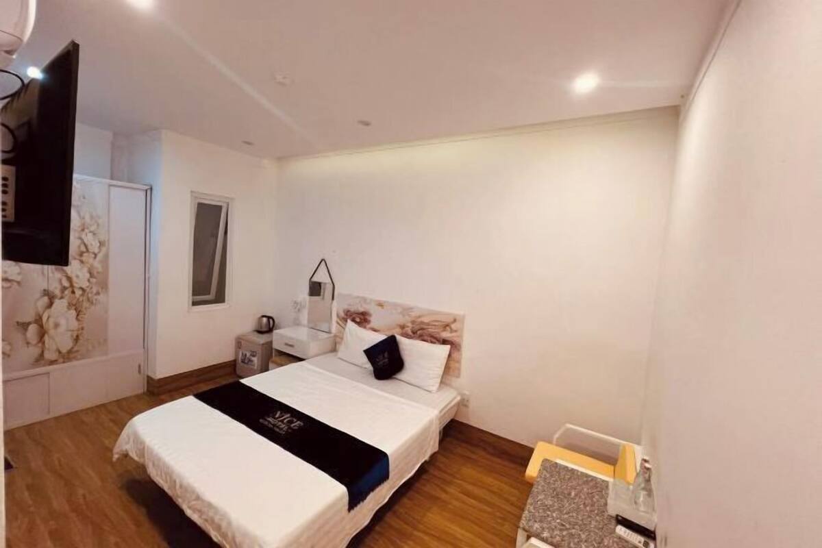 A bedroom with a bed, bedside table, lamp, and a TV mounted on the wall.