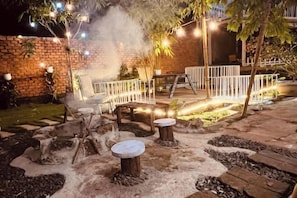An outdoor patio area with seating, a fire pit, and string lights.