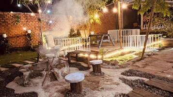 An outdoor seating area with stone tables and benches, surrounded by a brick wall and a white fence.