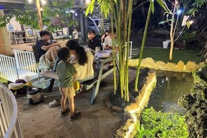 An outdoor dining area with tables and chairs, a small pond, and bamboo plants. - Nice Hotel Buon Ma Thuot (Tu An)