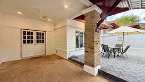 A covered patio area with a table and chairs, a door, and a stone pillar.