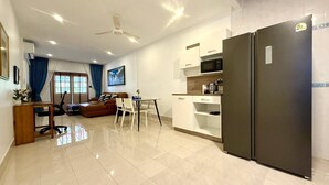 A modern living room with a sofa, a dining table, and chairs. There is a kitchen area with a refrigerator and a microwave.