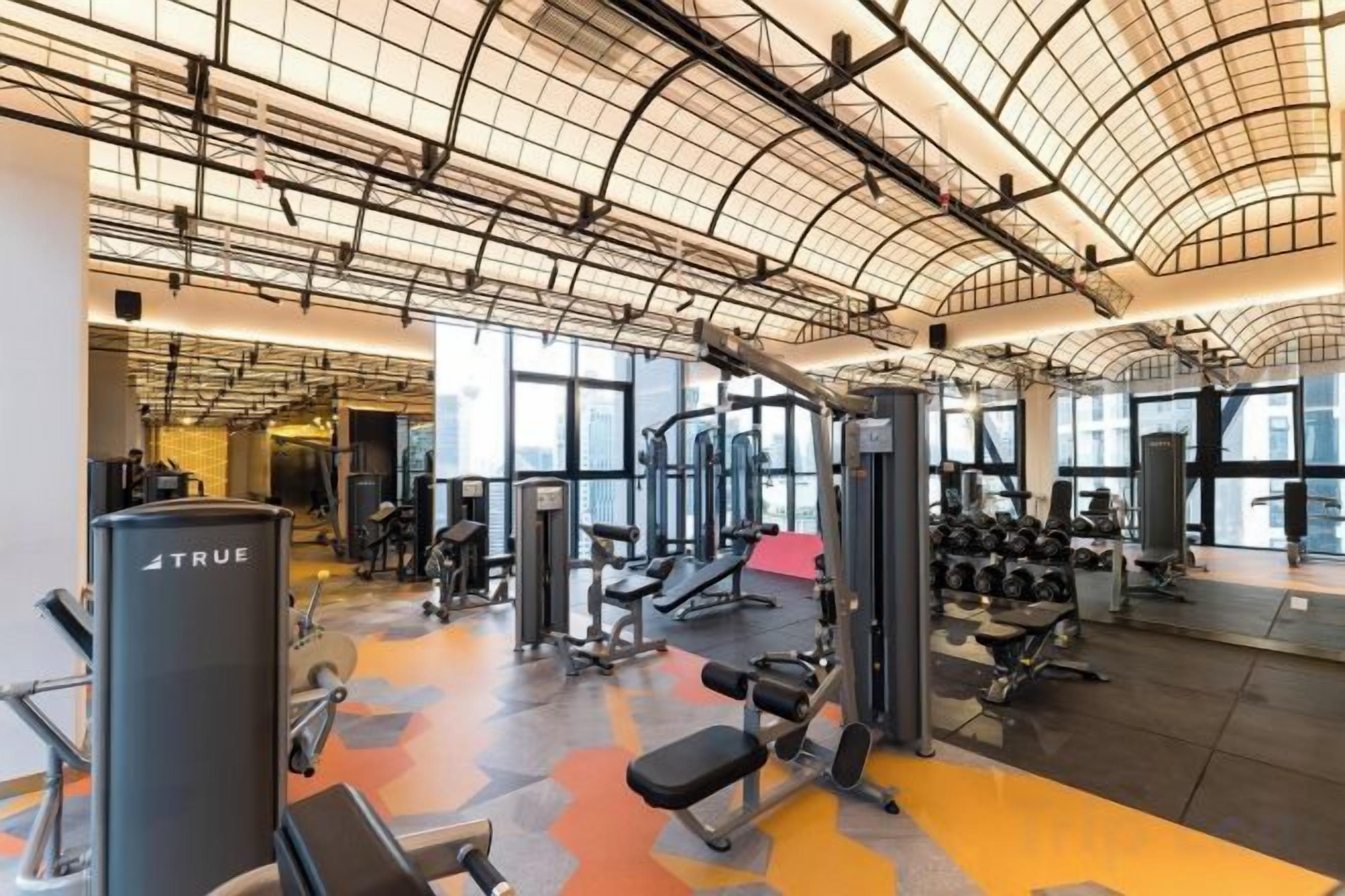 A gym with various exercise equipment, large windows, and a high ceiling.