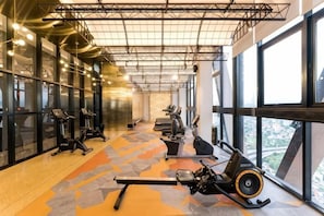 Un gimnasio con equipo de ejercicios, amplias ventanas y un techo alto.