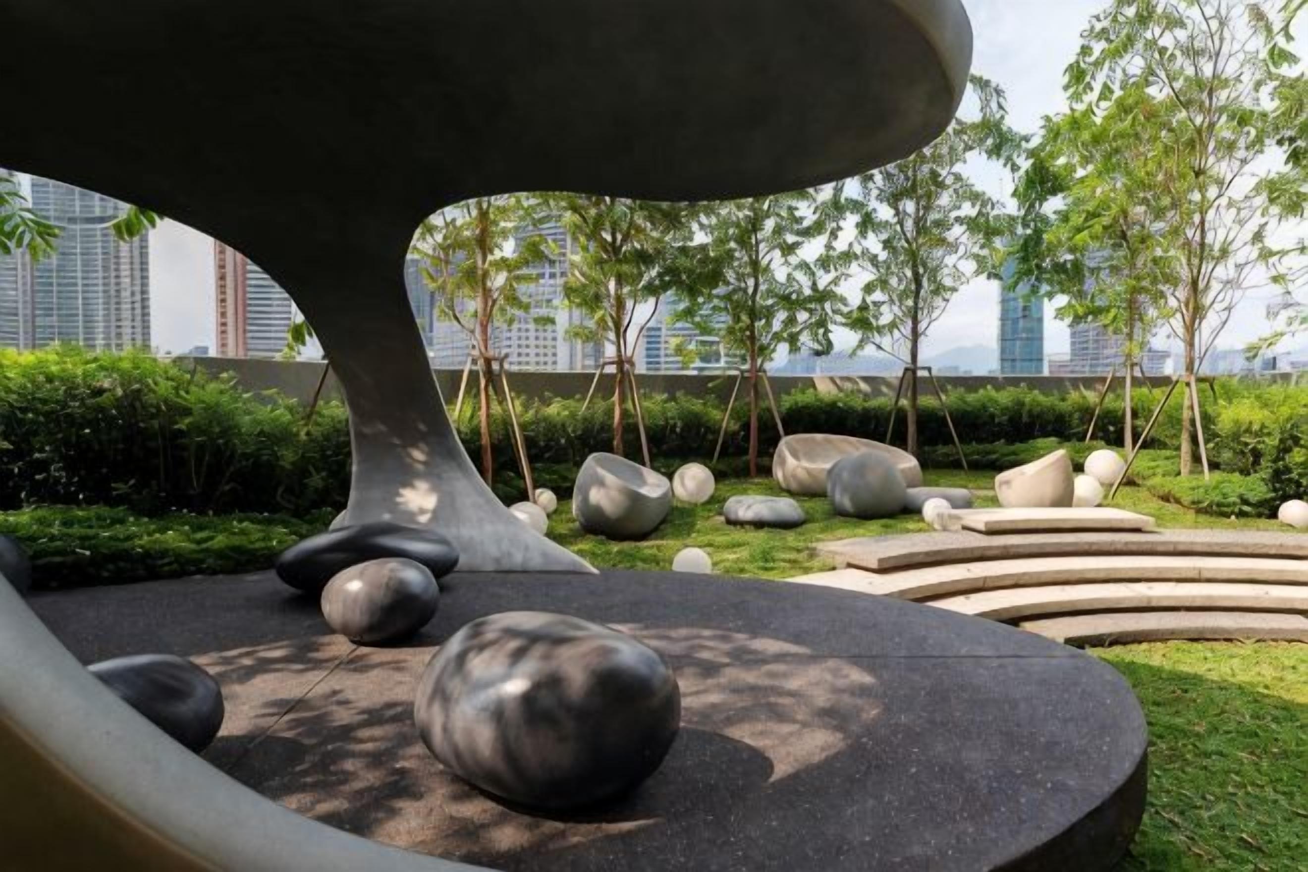 A landscaped area with a modern sculpture, large rocks, and a curved seating area.