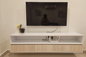 A flat-screen TV mounted on a white entertainment unit with a power strip and a small potted plant. - Grace Suite @ The Shore Kota Kinabalu (Kota Kinabalu)