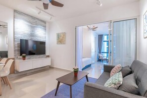Una sala de estar moderna con un sofá, una mesa de centro y un televisor de pantalla plana. Hay un comedor con una mesa y sillas, y una cocina con una encimera y armarios.