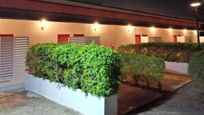 A building exterior at night with illuminated windows and a well-maintained garden area with hedges and shrubs. - Ingnaam Thajeen (Si Prachan)
