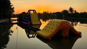 A water park with inflatable slides and a small building, set against a sunset. - Ingnaam Thajeen (Si Prachan)