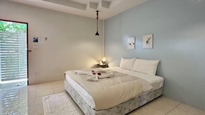 A bedroom with a bed, a nightstand, a wall-mounted lamp, and a door with blinds. - Ingnaam Thajeen (Si Prachan)