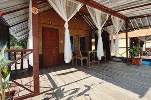 A covered outdoor area with a wooden floor, a door, and a table with chairs. - Ingnaam Thajeen (Si Prachan)