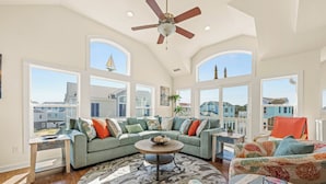 A spacious living room with a large window, a ceiling fan, and a view of the neighborhood.