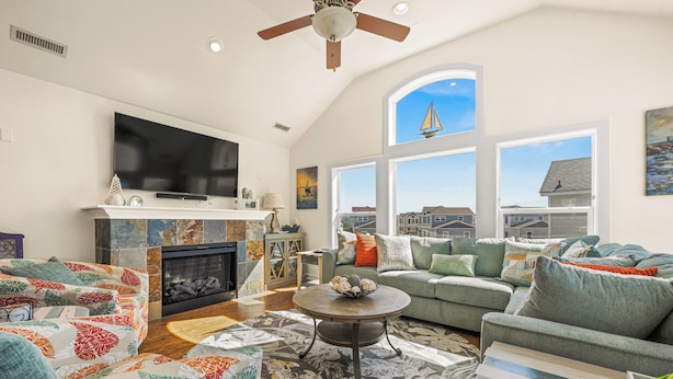 A spacious living room with a fireplace, comfortable seating, a flat-screen TV, and large windows offering a view of the city.