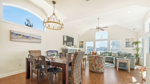 A spacious living area with a dining table, wicker chairs, a sofa, and a ceiling fan.