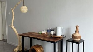 Un tavolo di legno con una macchina da caffè, tazze, bottiglie, un vaso e un ramo con una lampada a sospensione.