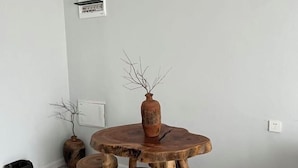 Un tavolo rotondo di legno con un vaso e rami, una parete bianca e un cestino nero.