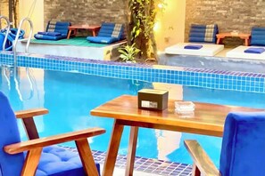 Un área de piscina con sillones de descanso y una mesa, rodeada por un muro de ladrillo y plantas.