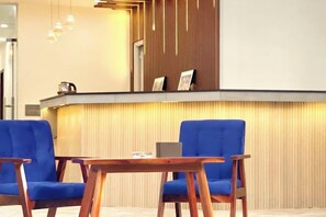 Een receptiegedeelte met een houten receptiebalie, twee blauwe stoelen en een laptop op het bureau.