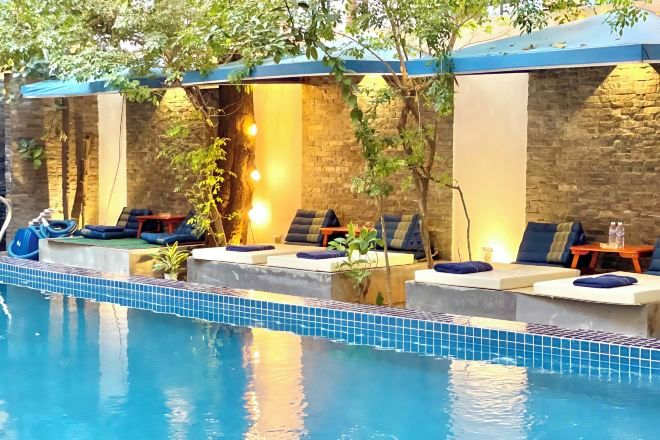 A pool area with lounge chairs and a small table, surrounded by stone walls and plants.