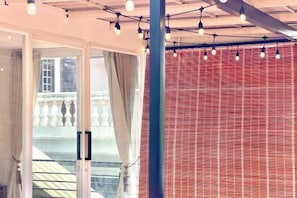 A room with a glass door leading to a balcony, a red brick wall, and string lights hanging from the ceiling.