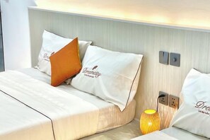 A hotel room with a bed, pillows, a lamp, and a wall-mounted switch.