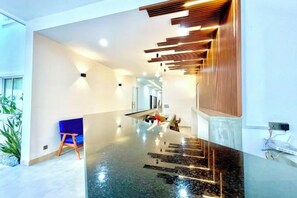 A modern interior with a reflective floor, wooden ceiling accents, and a seating area with a blue chair. - SKY VILLA - BKK Central Phnom Penh - Rooms and Apartments (Phnom Penh)