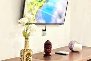 Un televisor de pantalla plana montado en la pared, un florero con flores sobre una mesa y un control remoto.