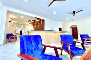 A modern hotel lobby with a reception desk, blue upholstered chairs, and a ceiling fan.