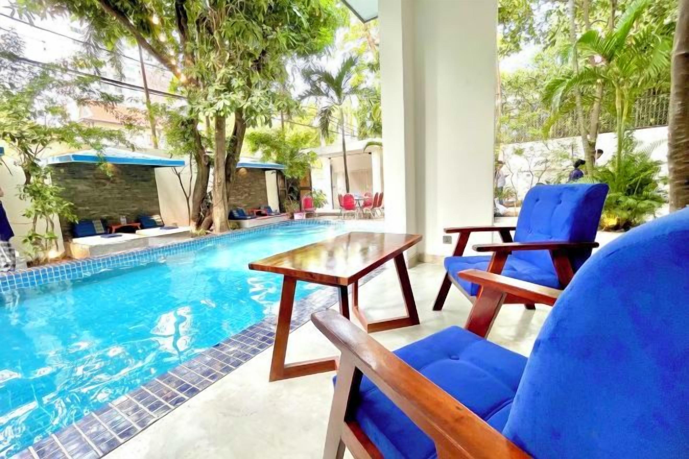 A pool area with a table and chairs, surrounded by greenery.