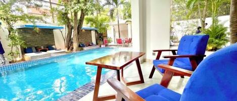 A pool area with a table and chairs, surrounded by greenery.