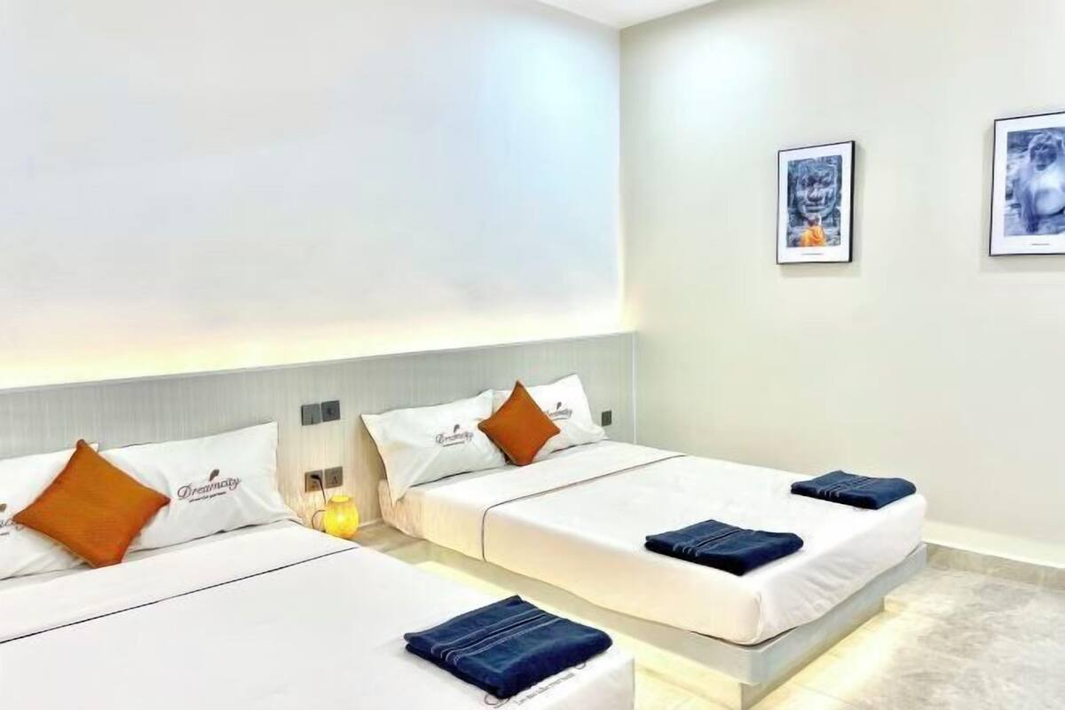 Ein Hotelzimmer mit zwei Betten, jeweils mit Kissen und Decke, einem Nachttisch mit Lampe sowie gerahmten Bildern an der Wand.