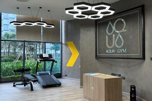 A gym with exercise equipment, a wooden cabinet, and a large window with a view of greenery. - The Cam Ranh Oceanview (Cam Ranh)