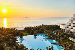 A resort with a large infinity pool surrounded by palm trees and a view of the ocean at sunset. - The Cam Ranh Oceanview (Cam Ranh)