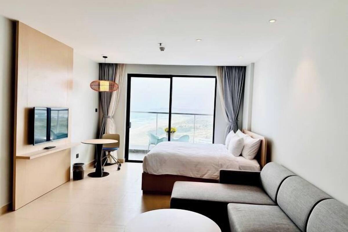 Une chambre d’hôtel moderne équipée d’un lit, d’un canapé, d’une télévision, d’une petite table et d’un balcon avec vue.