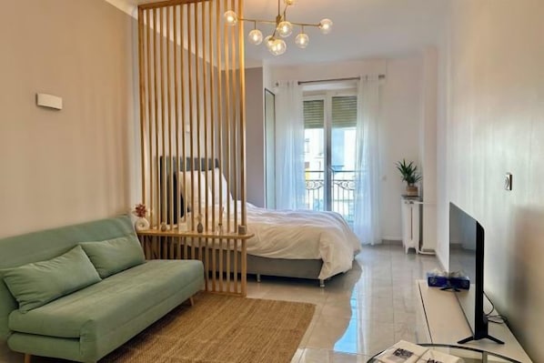 Une chambre à coucher moderne avec un lit, un canapé vert, une télévision et un élément de séparation décoratif.